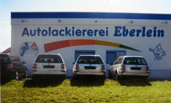 Betriebsgebäude der Autolackiererei Eberlein mit Firmenschriftzug und davor parkenden Autos
