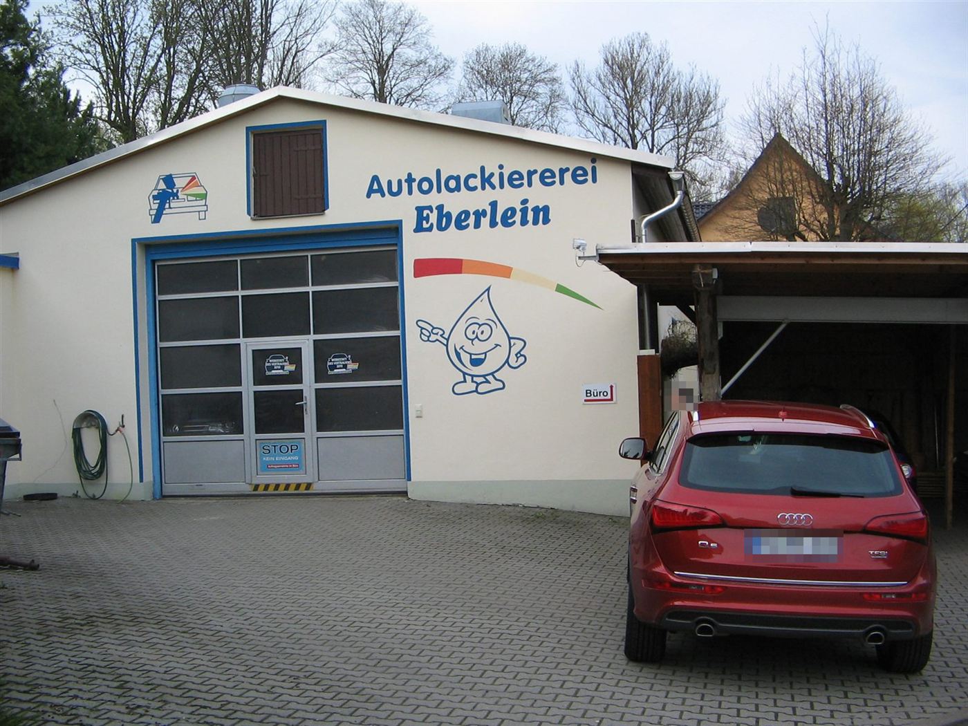 Werkstattgebäude mit Firmenschriftzug und Lacktropfen-Maskottchen