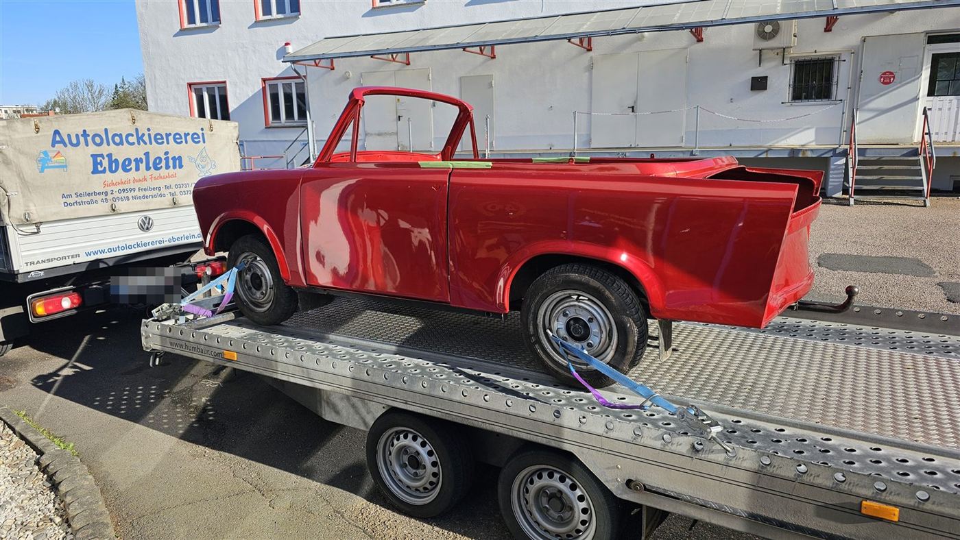 Rot lackierter Trabant auf dem Autotransporter vor dem Firmengebäude